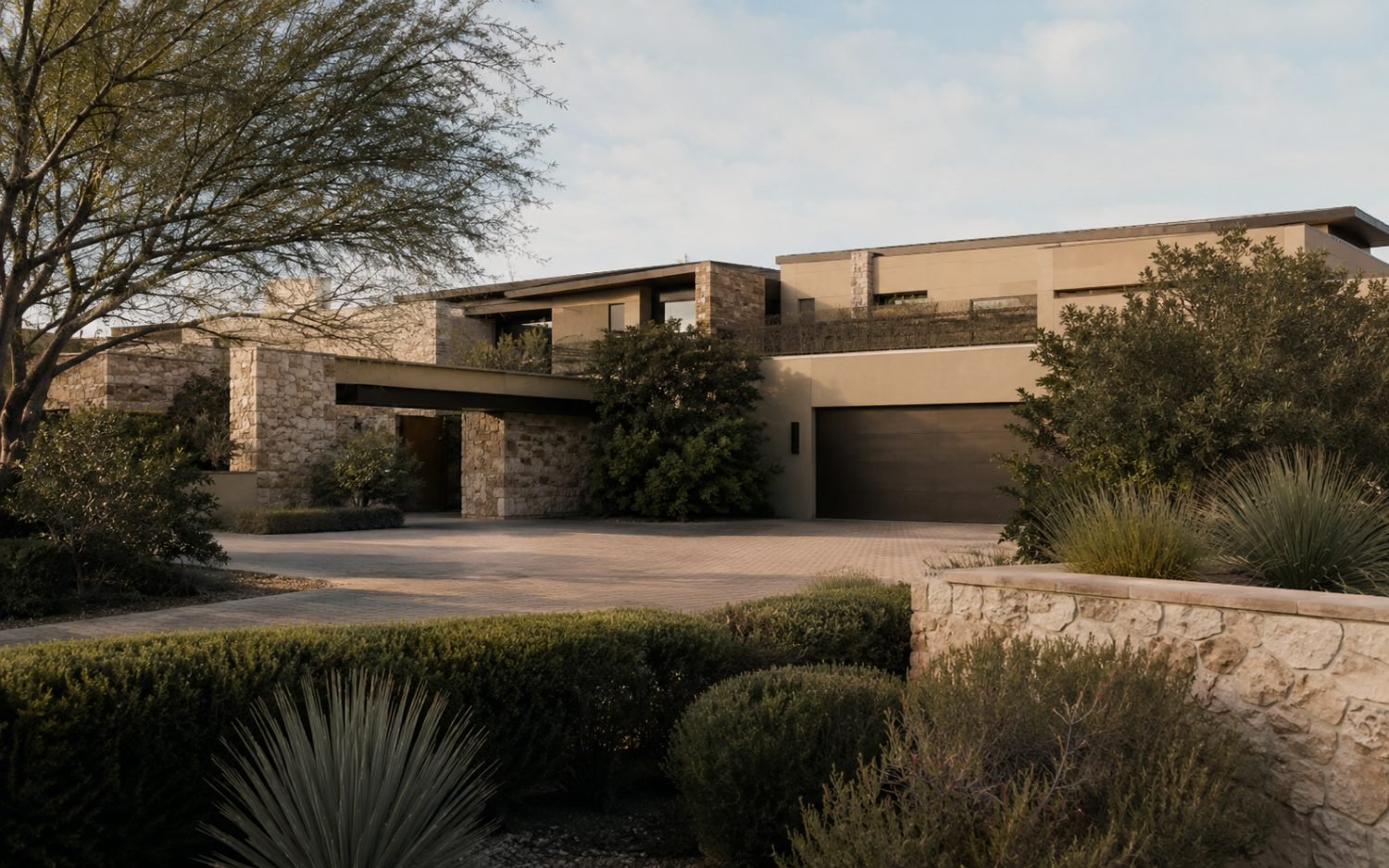 A contemporary stone-and-stucco estate set behind mature landscaping at golden hour.